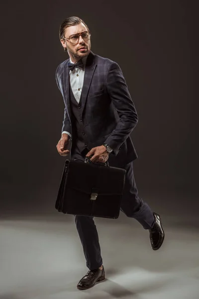 Hombre de negocios serio con maletín corriendo y mirando hacia otro lado en negro - foto de stock