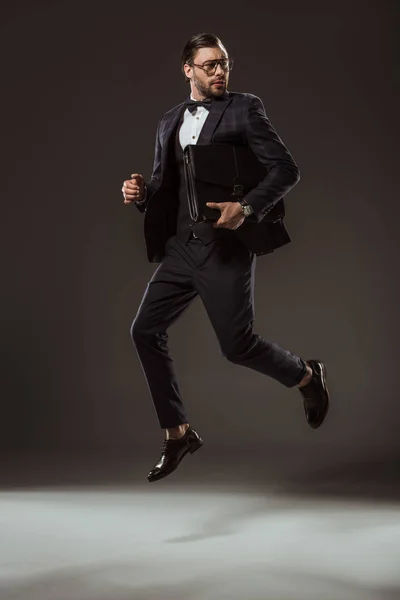 Elegante uomo d'affari con valigetta che salta e distoglie lo sguardo sul nero — Foto stock