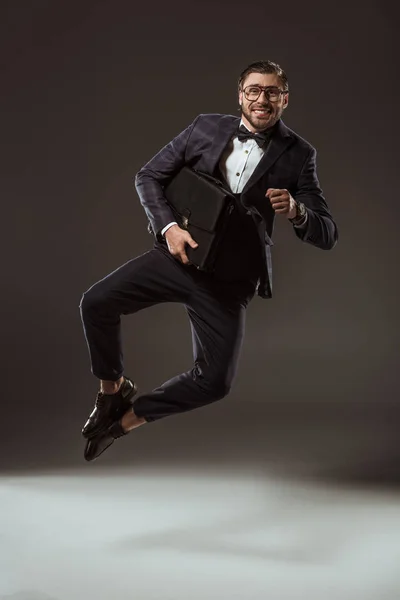 Empresário animado com pasta pulando e olhando para a câmera em preto — Fotografia de Stock