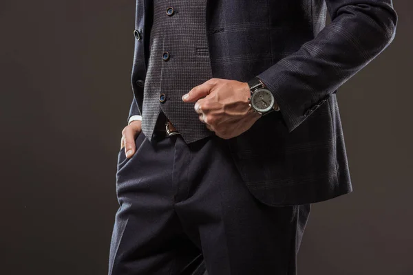 Cropped shot of man in stylish suit wearing wristwatch and standing with hand in pocket isolated on black — Stock Photo