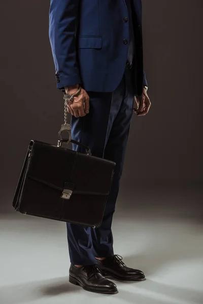 Обрізаний знімок бізнесмена в наручниках з портфелем на чорному — стокове фото