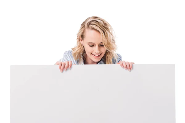 Усміхнена приваблива жінка дивиться на порожній плакат ізольовано на білому — стокове фото