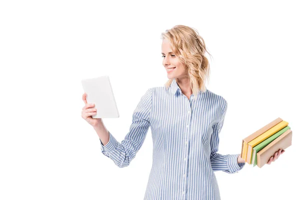 Smiling attractive woman looking at tablet and holding books isolated on white — Stock Photo