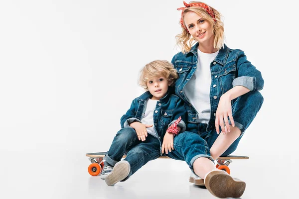 Mãe e filho sentado no skate e olhando para a câmera no branco — Fotografia de Stock