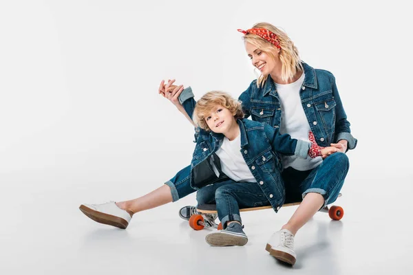 Heureux mère et fils assis sur skateboard et tenant la main sur blanc — Photo de stock