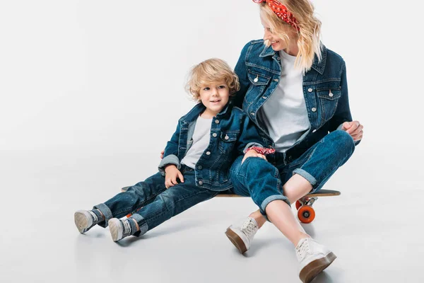 Smiling mother and son sitting on skateboard on white — Stock Photo