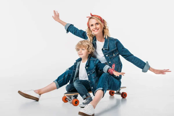 Glückliche Mutter und Sohn auf Skateboard sitzen und so tun, als ob sie auf Weiß fliegen — Stockfoto