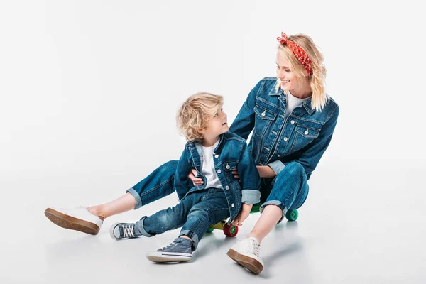 Mère et fils assis sur skateboard et se regardant sur blanc — Photo de stock