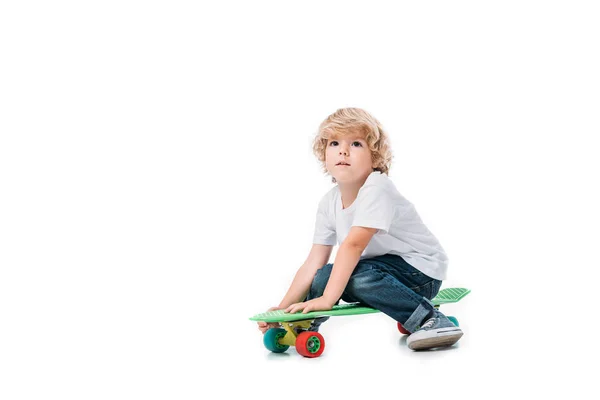 Adorável menino sentado no skate isolado no branco — Fotografia de Stock