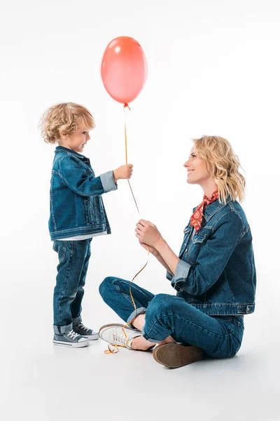 Vista lateral del hijo presentando globo rojo a la madre en blanco - foto de stock