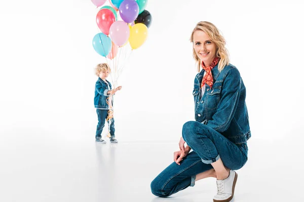 Hijo caminando con globos y madre en cuclillas en primer plano en blanco - foto de stock