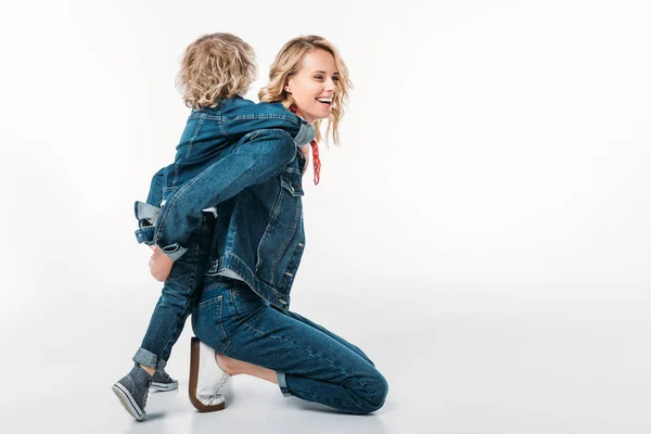 Seitenansicht einer glücklichen Mutter, die ihrem Sohn Huckepack auf Weiß gibt — Stockfoto