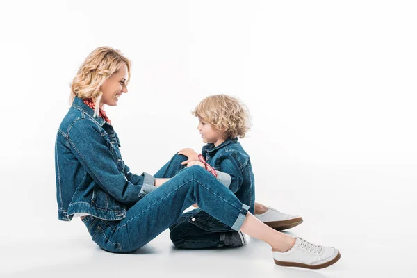 Vista lateral de mãe sorridente e filho sentado no chão no branco — Fotografia de Stock