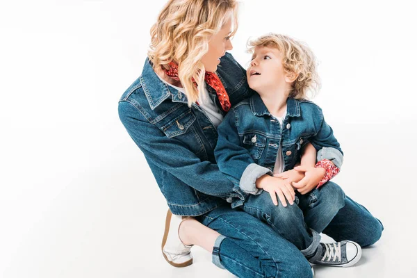 Smiling mother and son squatting and looking at each other isolated on white — Stock Photo