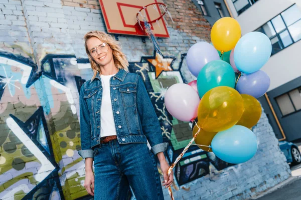 Donna sorridente in piedi sulla strada con fascio di palloncini — Foto stock