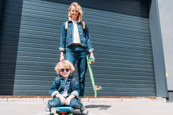 Feliz madre e hijo con patinetas en la calle - foto de stock