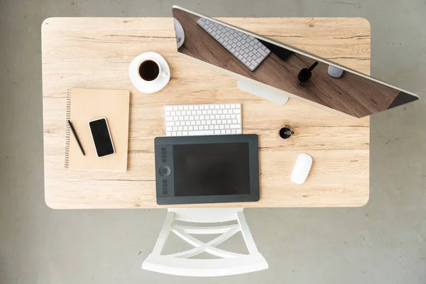 Top view of workplace with computer, smartphone, graphic tablet and coffee cup on table in office — Stock Photo