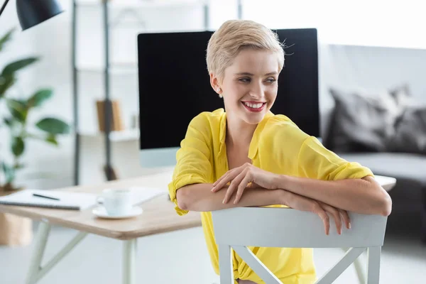 Enfoque selectivo de la mujer de negocios sonriente sentada cerca de la mesa con el ordenador en la oficina - foto de stock