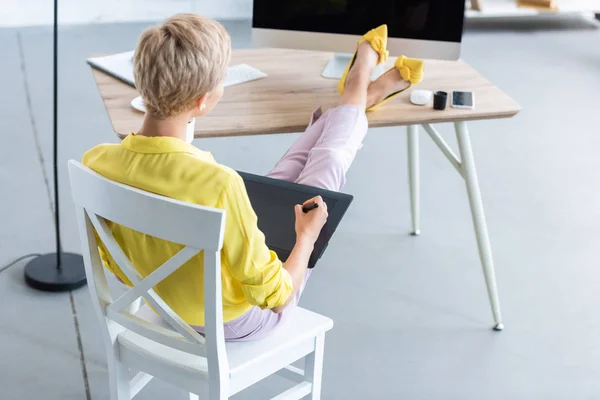 Visão traseira de freelancer feminino trabalhando em tablet gráfico à mesa com computador no escritório em casa — Fotografia de Stock