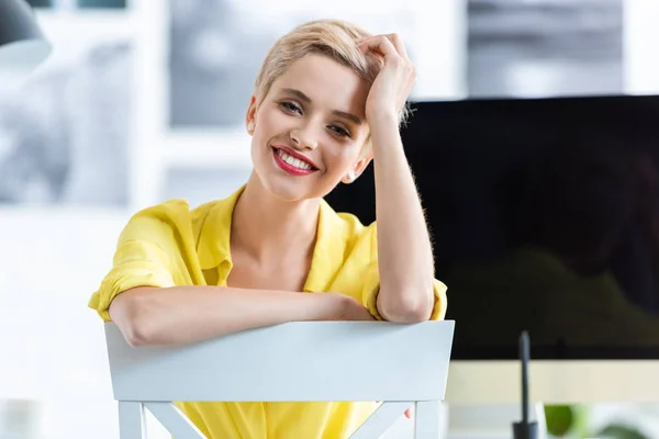 Lächelnde Geschäftsfrau sitzt auf Stuhl und blickt im Büro in die Kamera — Stockfoto