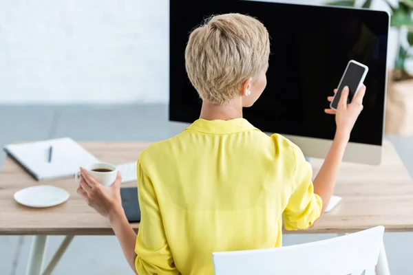 Rückansicht einer Geschäftsfrau, die im Büro Kaffee trinkt und ihr Smartphone checkt — Stockfoto