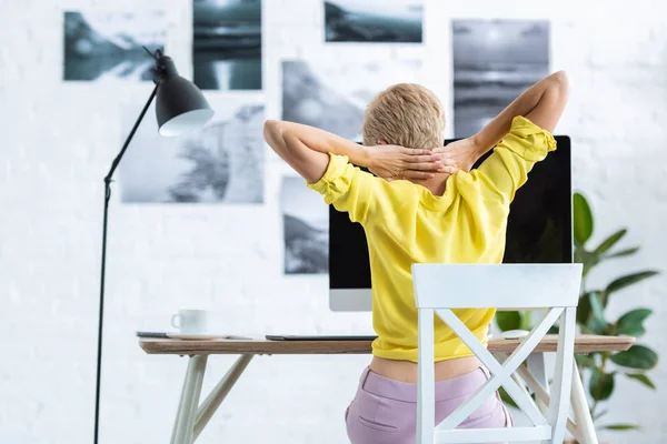 Vista trasera de la mujer de negocios haciendo estiramiento mientras está sentado en la mesa con el ordenador en casa - foto de stock