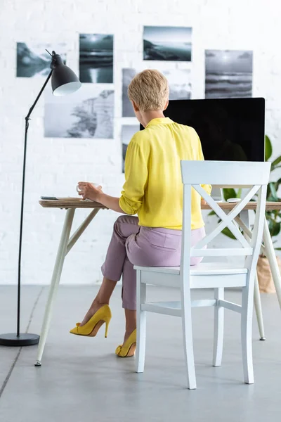 Vue arrière de femme d'affaires buvant du café et travaillant sur ordinateur à table — Photo de stock