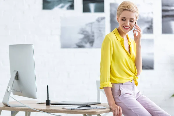 Female freelancer talking on smartphone near table with graphic tablet and computer at home office — Stock Photo