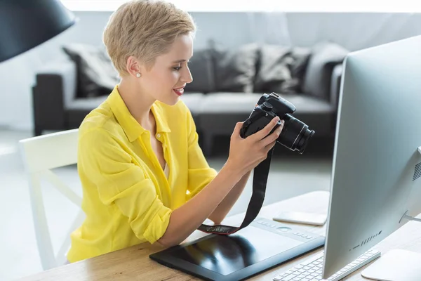 Visão lateral do fotógrafo feminino olhando para a tela da câmera na mesa com tablet gráfico e computador — Fotografia de Stock