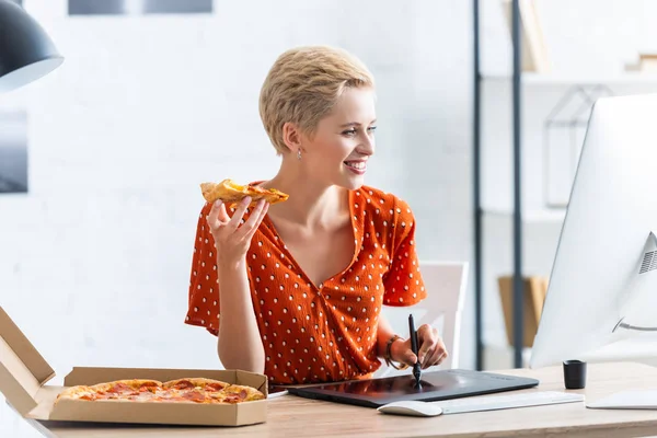 Sorrindo freelancer feminino comer pizza e desenho em tablet gráfico em casa escritório — Fotografia de Stock