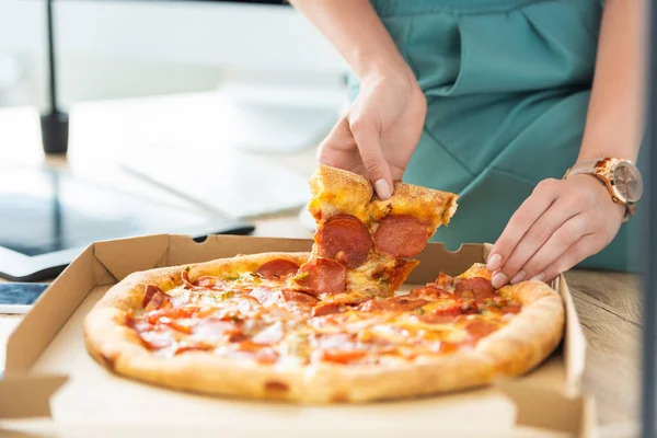 Vue partielle d'une pigiste féminine prenant une tranche de pizza à table avec tablette graphique — Photo de stock