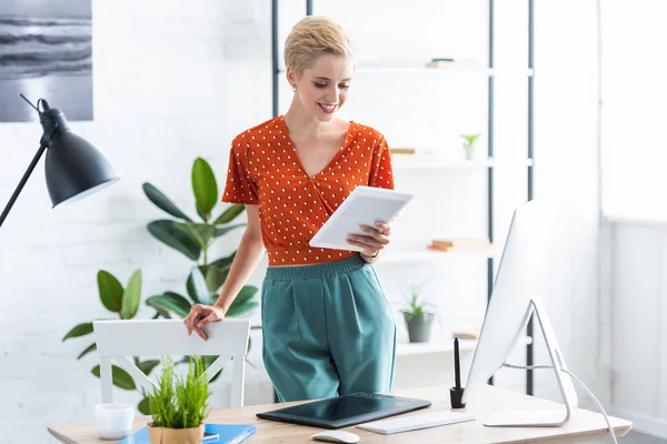 Freelancer femenina usando tableta digital cerca de la mesa con computadora en la oficina en casa - foto de stock