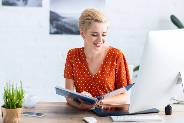 Libro di lettura femminile freelance sorridente a tavola con tablet grafico e computer in home office — Foto stock