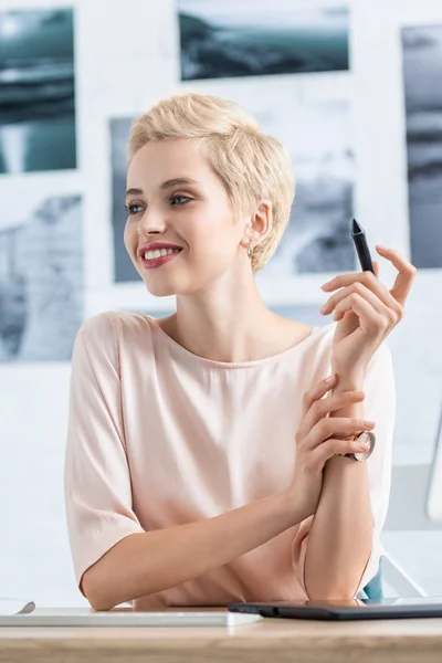Portrait of happy female freelancer looking away at table with graphic tablet in home office — Stock Photo