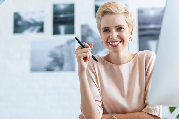 Souriant femelle pigiste tenant stylo pour tablette graphique dans le bureau à domicile — Photo de stock