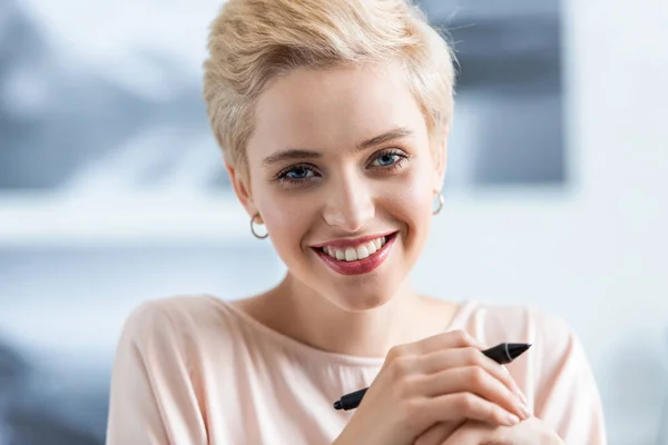 Primer plano retrato de sonriente mujer atractiva sosteniendo pluma para tableta gráfica - foto de stock