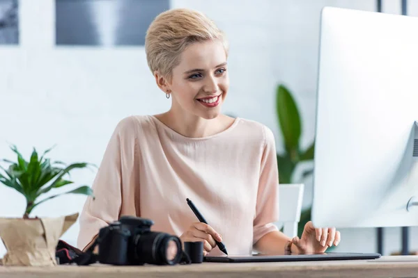 Female photographer drawing on graphic tablet at table with computer and photo camera in home office — Stock Photo
