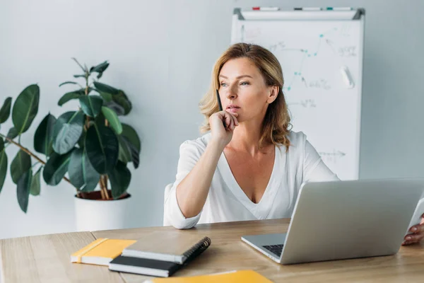 Mulher de negócios atraente pensativo sentado à mesa com laptop no escritório e olhando para longe — Fotografia de Stock