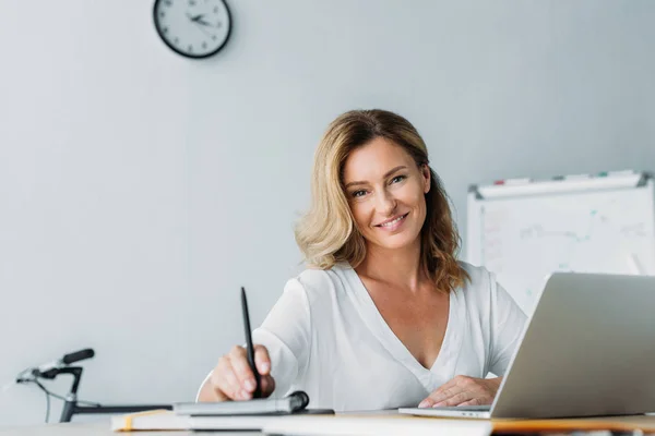 Attraktive Geschäftsfrau mit Stift und Blick in die Kamera im Büro — Stockfoto