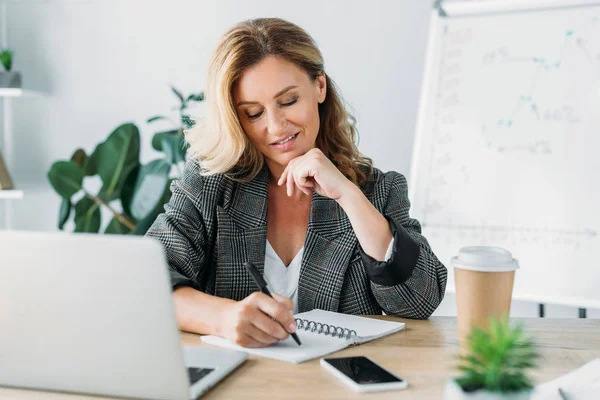 Attractive businesswoman writing something to notebook in office — Stock Photo