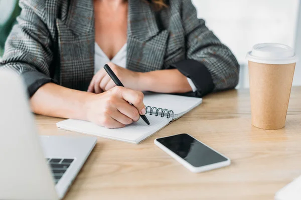 Imagen recortada de la mujer de negocios escribiendo algo a cuaderno en la oficina - foto de stock