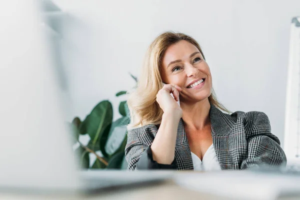 Lächelnde attraktive Geschäftsfrau, die im Büro per Smartphone spricht — Stockfoto