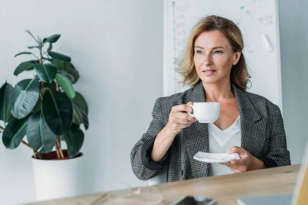 Attrayant femme d'affaires tenant tasse de café au bureau — Photo de stock