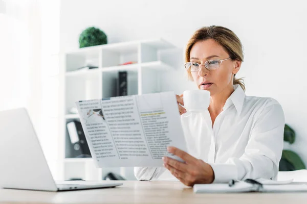 Привлекательная деловая женщина пьет кофе и читает газеты в офисе — стоковое фото