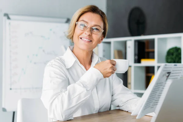 Приваблива бізнес-леді тримає чашку кави і дивиться в офіс — стокове фото