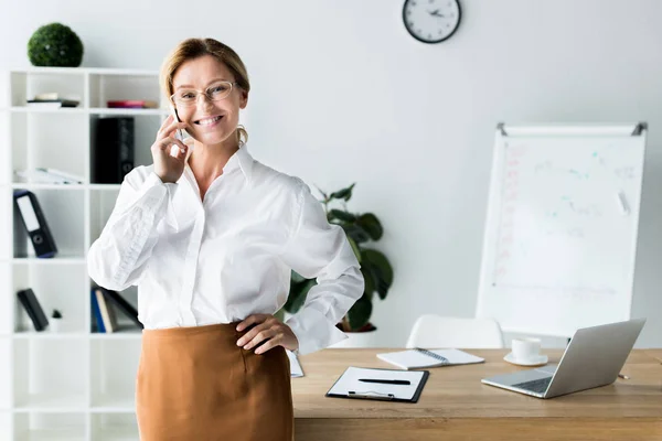 Усміхнена приваблива бізнес-леді розмовляє по смартфону в офісі — стокове фото