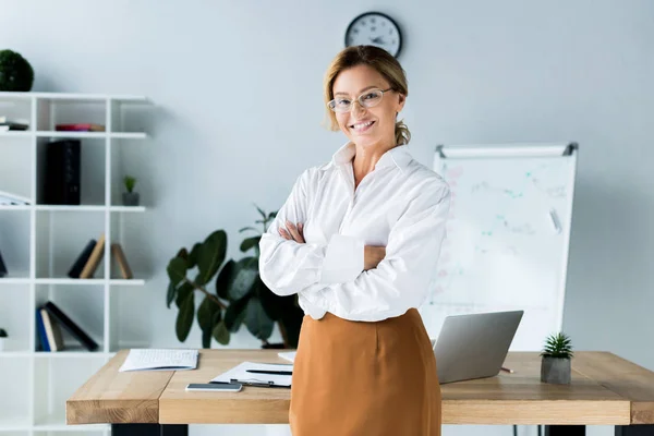 Atractiva mujer de negocios de pie con los brazos cruzados en la oficina - foto de stock