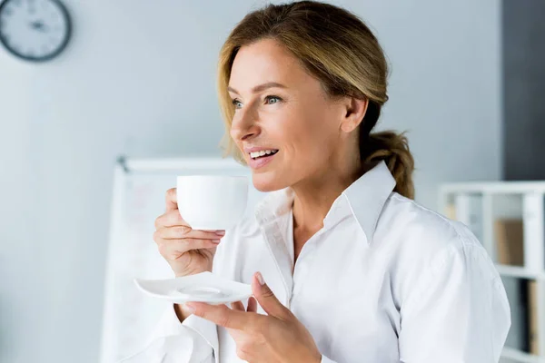 Sonriente atractiva empresaria bebiendo café en la oficina - foto de stock