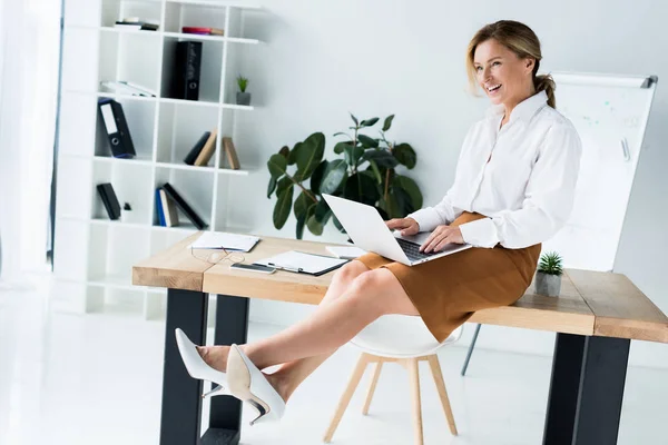 Vista lateral de mulher de negócios atraente sentado com laptop na mesa no escritório — Fotografia de Stock