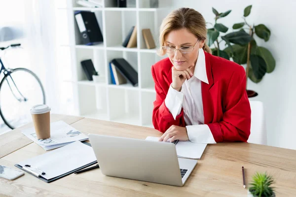 Atractiva mujer de negocios mirando portátil en la oficina - foto de stock